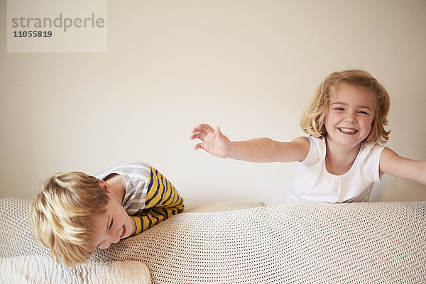Zwei Kinder spielen hinter einem Sofa  ein Junge und ein Mädchen lachen.