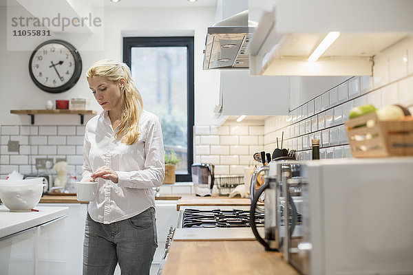 Eine Frau  die in einer modernen Küche eine Tasse Tee zubereitet.