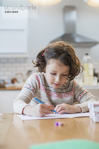 Ein Mädchen sitzt an einem Küchentisch und schreibt eine Karte oder einen Brief.