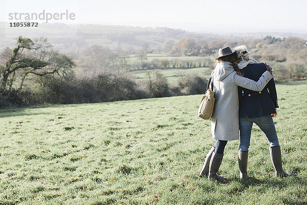 Zwei Frauen nebeneinander auf einem Grashang mit Blick auf die Landschaft von Dorset.