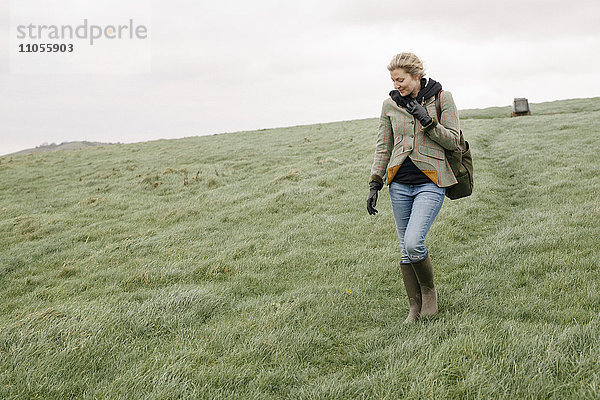 Eine Frau in warmem Mantel und Handschuhen  die über offenes Land  Grasland und Moore geht.