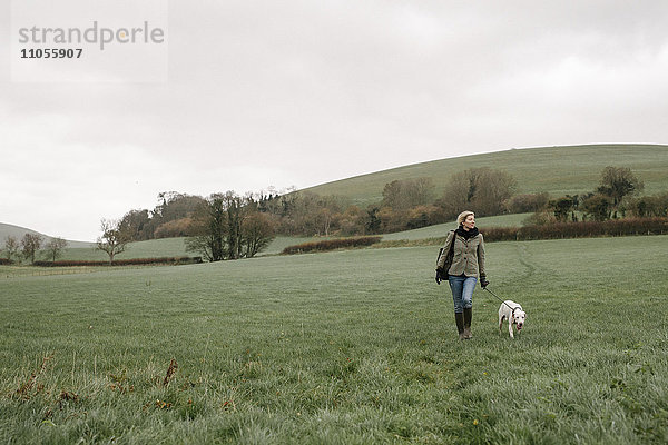 Eine Frau geht mit einem Hund über ein Grasfeld.