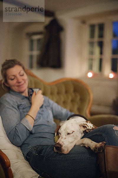 Eine auf einem Sofa sitzende Frau mit einem großen Hund mit dem Kopf auf ihrem Schoß.