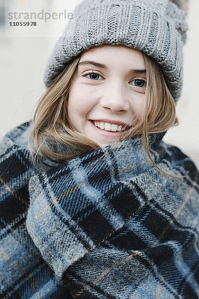 Ein junges Mädchen mit Schottenkaro-Schal und Wollmütze im Winter im Freien.