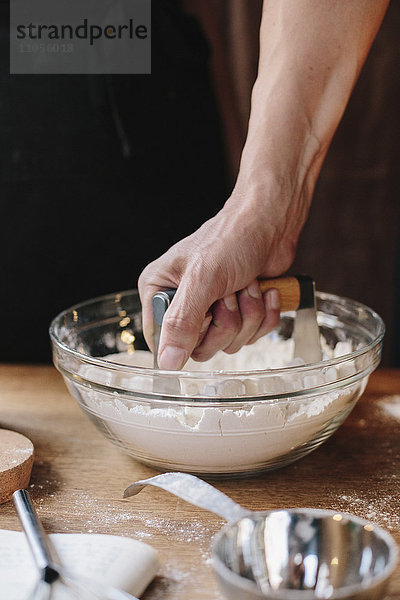 Eine Person  die einen Stampfer benutzt  um Butter in einer Schüssel zu erweichen und den Teig zu mischen.