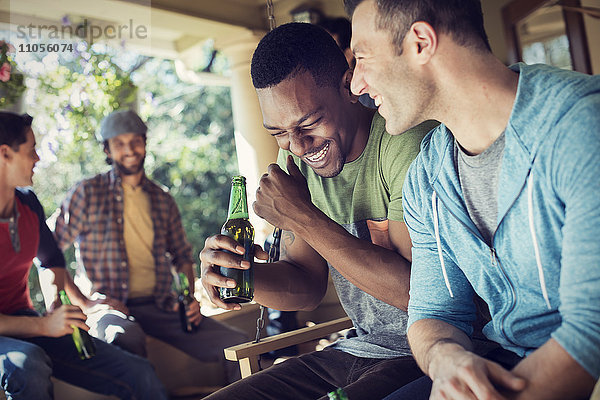 Eine Gruppe von Freunden  Männern und Frauen bei einer Hausparty. Zwei Männer lachen.
