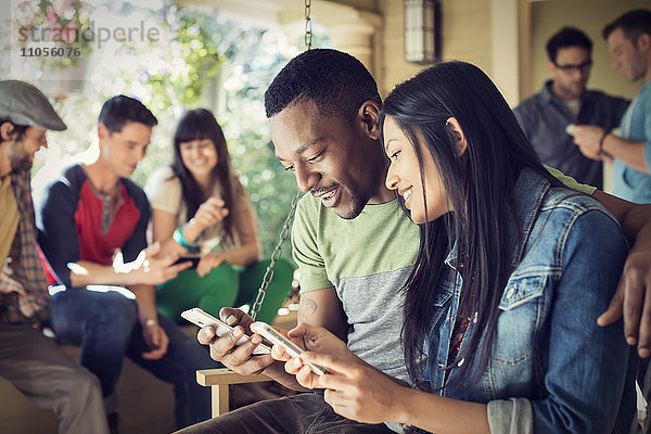 Eine Gruppe von Freunden  Männer und Frauen auf einer Hausparty  ein Paar  das seine Smartphones überprüft.
