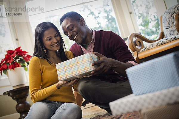 Ein Paar auf einem Sofa  das eingepackte Geschenke austauscht.