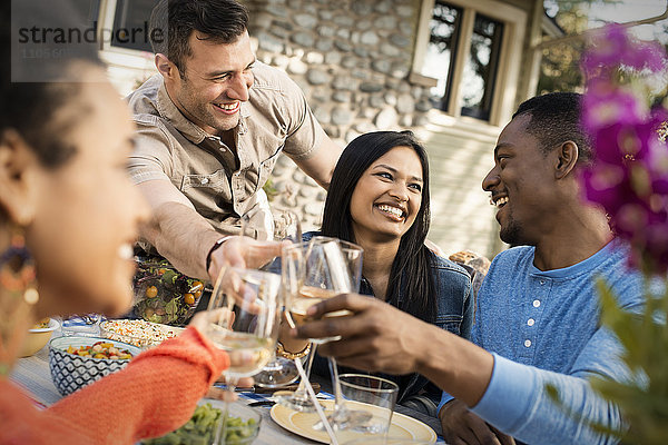 Freunde an einem Tisch  Männer und Frauen lachen und stoßen mit einem Weinglas an.