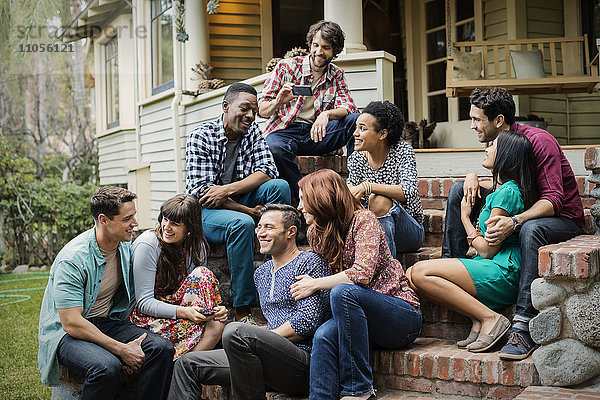 Eine Gruppe von Freunden sitzt auf den Stufen einer Hausveranda  unterhält sich und lacht.