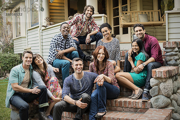 Eine Gruppe von Freunden sitzt auf den Stufen einer Hausveranda  posiert und lacht.