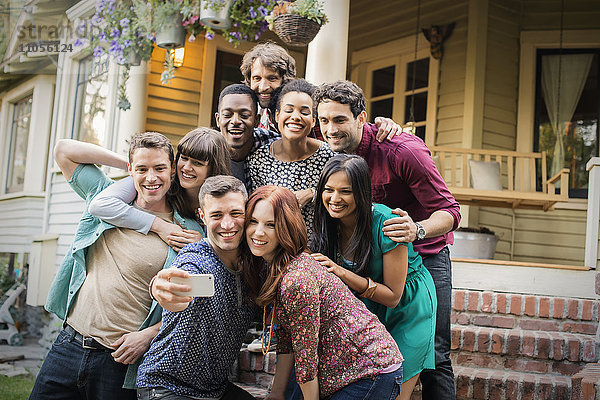 Eine Gruppe von Freunden posiert auf den Stufen einer Hausveranda und nimmt eine Gruppe selbst in die Hand.