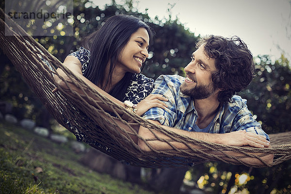 Ein Paar  ein junger Mann und eine Frau liegen in einer großen Hängematte im Garten.