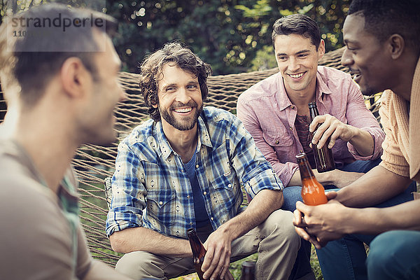 Eine Gruppe von Freunden  die sich in einer großen Hängematte im Garten bei einem Bier ausruhen.