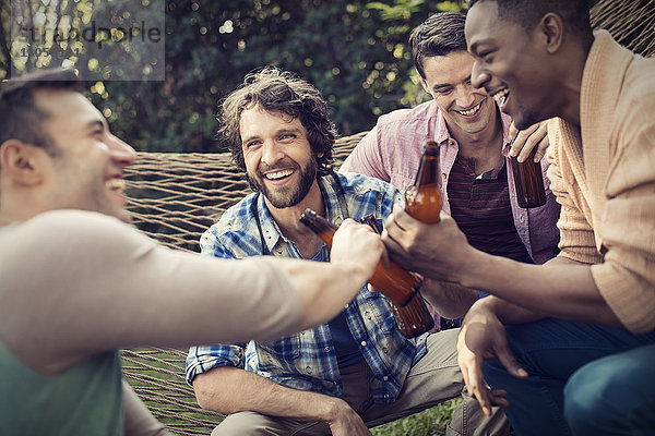 Eine Gruppe von Freunden  die sich in einer großen Hängematte im Garten bei einem Bier ausruhen.