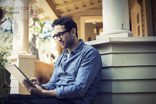 Ein Mann sitzt entspannt in einer ruhigen Ecke einer Veranda und benutzt ein digitales Tablet.