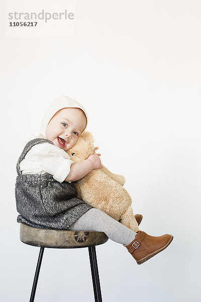 Ein kleines Kind  ein Mädchen  das auf einem hohen Hocker sitzt und einen Teddybär hält.