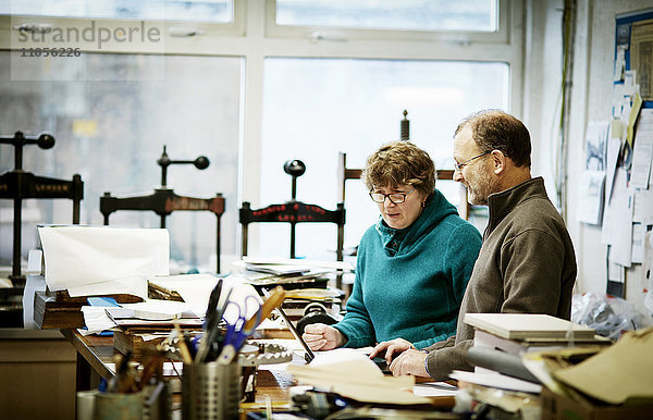 Zwei Personen arbeiten in einer Buchbinderei. Umgeben von Werkzeugen und Buchpressen.