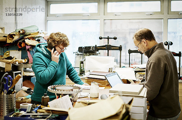 Eine Frau nimmt einen Telefonanruf entgegen und ein Mann arbeitet an einem Laptop-Computer in einer Buchbinderei.