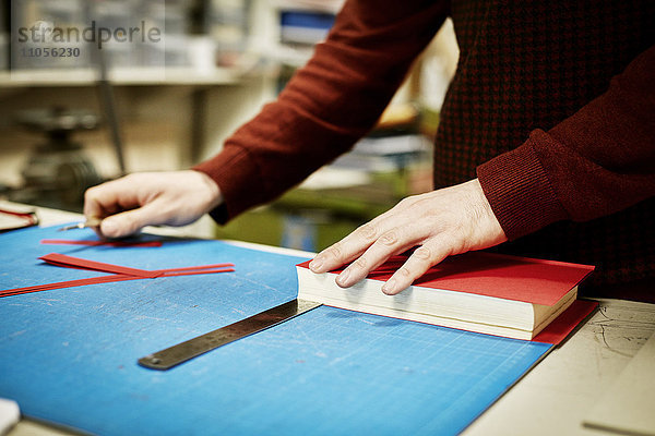 Ein Mann  der in einer Buchbinderei auf einer Werkbank arbeitet  um das Material für die Wiedergewinnung eines Buches zu messen und zu schneiden.