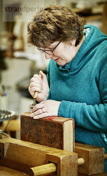 Eine Frau  die mit einem Handwerkzeug am Rücken eines gebundenen Buches arbeitet.