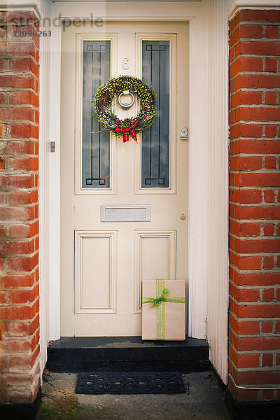 Weihnachtsschmuck. Ein Weihnachtskranz mit einer roten Schleife an der Haustür eines Hauses.