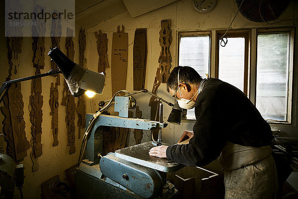Ein Mann  der in der Werkstatt eines Möbelherstellers arbeitet und eine Maschinensäge benutzt.