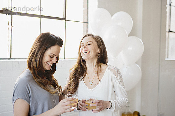 Zwei Frauen stehen nebeneinander und halten Getränke. Weiße Luftballons  Partydekoration.