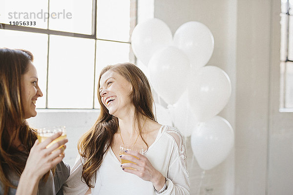 Zwei Frauen stehen nebeneinander und halten Getränke. Weiße Luftballons  Partydekoration.