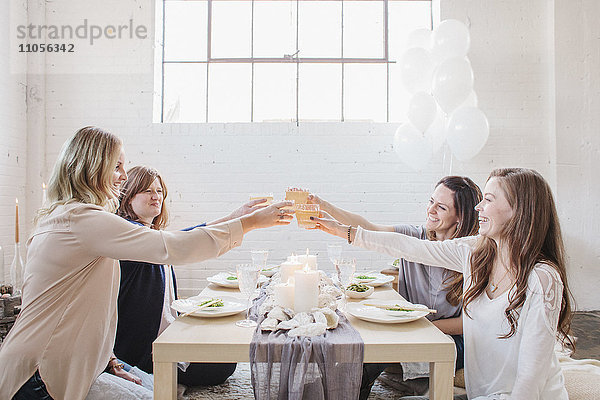 Vier Frauen saßen an einem niedrigen Tisch und erhoben ihre Gläser  um auf einander anzustoßen.