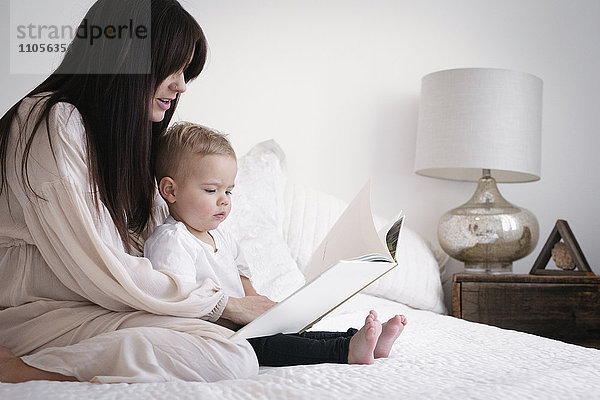 Eine hochschwangere Frau spielt mit ihrem kleinen Sohn. Sie sitzt auf einem Bett und liest eine Geschichte.