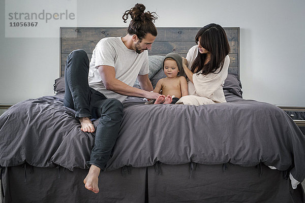 Ein junges Paar und ihr kleiner Sohn sitzen zusammen auf ihrem Bett.