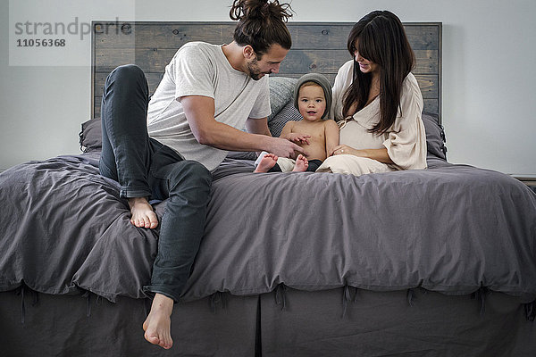 Ein junges Paar und ihr kleiner Sohn sitzen zusammen auf ihrem Bett.