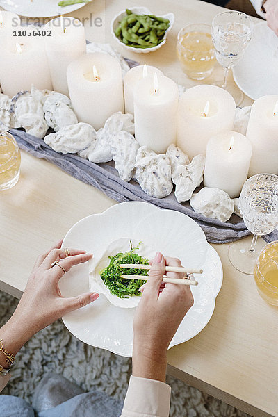 Draufsicht auf einen Tisch mit Kerzen und eine Person  die mit Stäbchen grünes Gemüse isst.