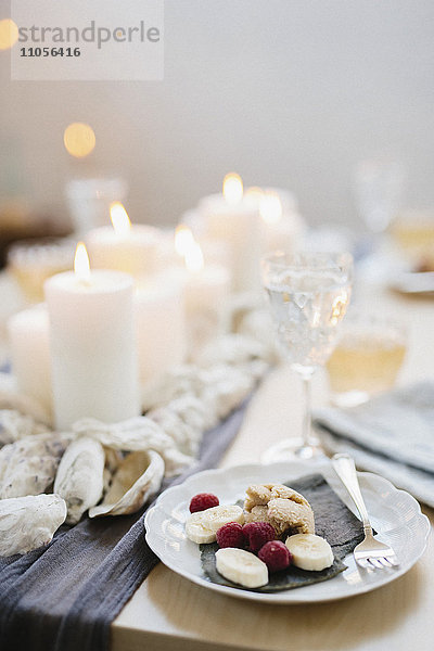 Ein Tisch für ein Festmahl mit gefüllten Weingläsern und Obsttellern und angezündeten Kerzen in der Mitte des Tisches.