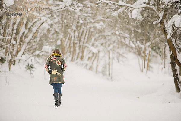 Eine Frau  die im Schnee im Wald spazieren geht.