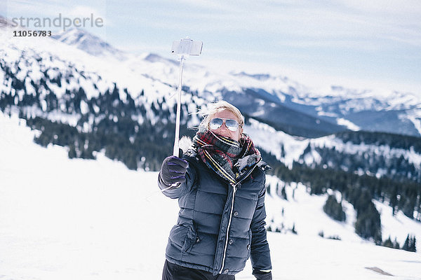 Eine Frau auf der Skipiste  die ihr Smartphone zum Fotografieren in die Hand nimmt.