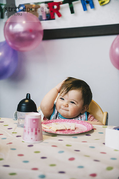 Ein Kind  ein einjähriges Mädchen auf seiner Geburtstagsfeier  das in einem Hochstuhl an einem Tisch sitzt.