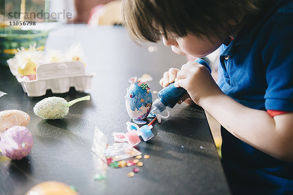 Ein Kind schmückt zu Ostern Eier mit Glitzer  Kleber und Farbe.