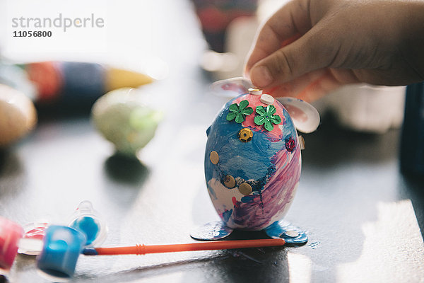 Ein Kind schmückt zu Ostern Eier mit Glitzer  Kleber und Farbe.