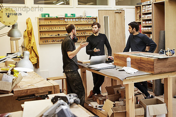 Eine Möbelwerkstatt  die maßgeschneiderte zeitgenössische Möbelstücke unter Verwendung traditioneller Fertigkeiten im modernen Design herstellt. Drei Personen an einem Tisch  die einen Plan besprechen.