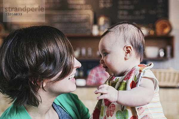 Eine Mutter und ein kleines Baby  die sich in einem Café gegenseitig anstarren und lächeln.