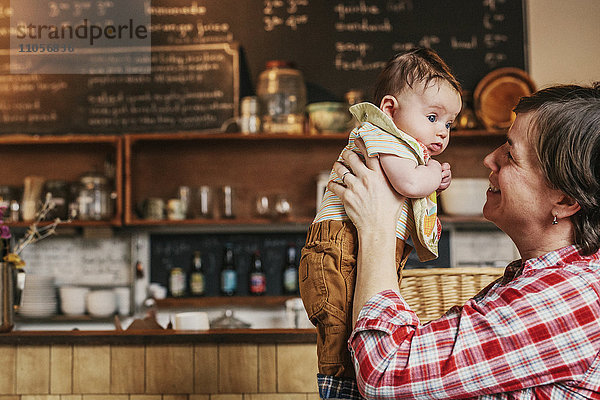 Eine Frau  die in einem Café ein kleines Baby hochhält.