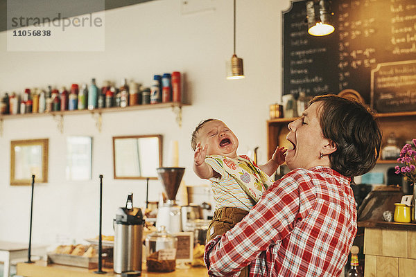 Eine Frau  die in einem Café ein weinendes Baby hält.