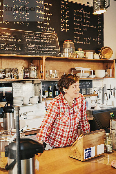 Eine Frau in einem karierten Hemd  die in einem Café hinter der Theke arbeitet.