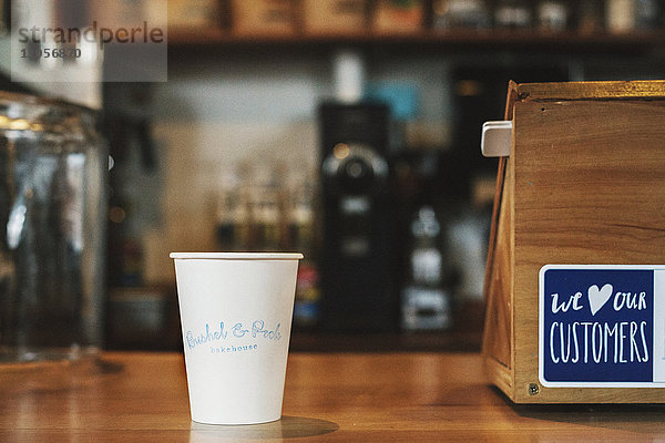 Ein Papierbecher mit dem Namen des Cafés und einem Schild auf der Theke.