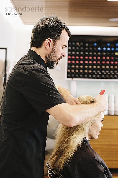 Ein Friseur  der die Haare eines Kunden auskämmt.