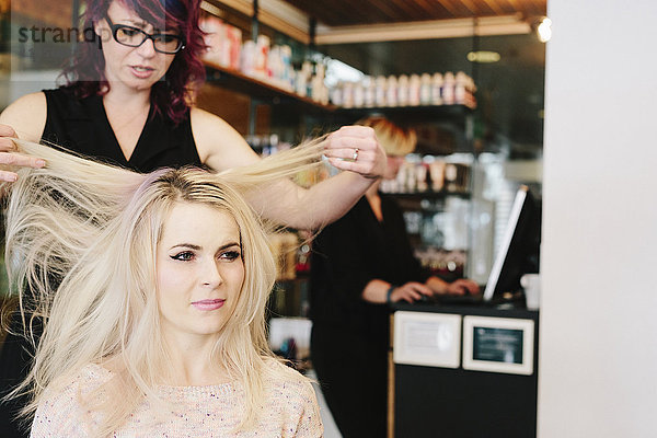 Ein Friseur und eine Kundin  eine junge Frau mit langen blonden Haaren  in einem Friseursalon.