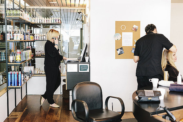 Ein Friseur  der an den Haaren eines Kunden arbeitet  und eine Frau am Telefon  die auf einen Laptop-Computer schaut.