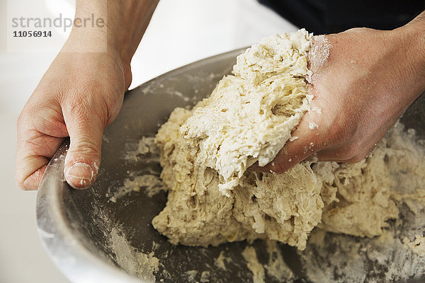 Nahaufnahme eines Bäckers  der Brotteig in einer Rührschüssel aus Metall knetet.